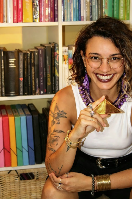 Vanesa smiling in front of her bookshelf, holding a small golden pyramid