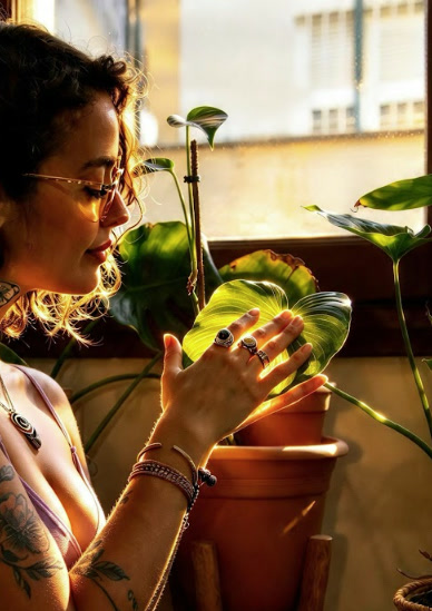 Vanesa backlit by the window, gently holding a plant leaf
